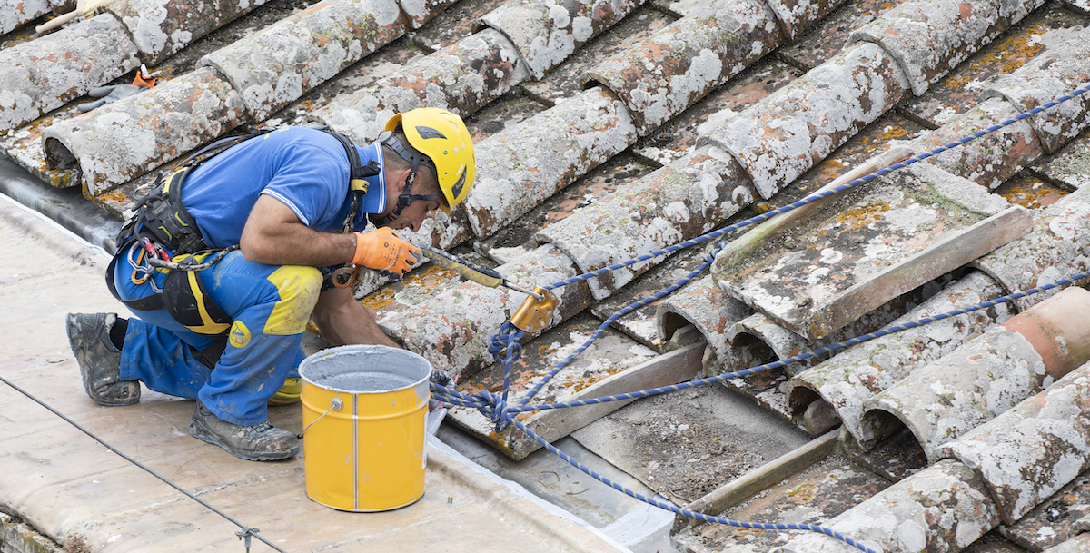 Esempio di operaio di EdiliziAcrobatica che lavora su un tetto e analizza per sostituzione eventuali tegole rotte