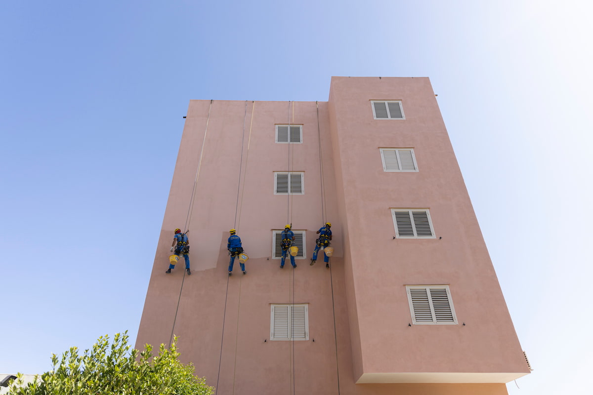 Condizioni di lavoro in condominio rosa con quattro operai sospesi su funi per lavori di ristrutturazione, orario lavori condominio