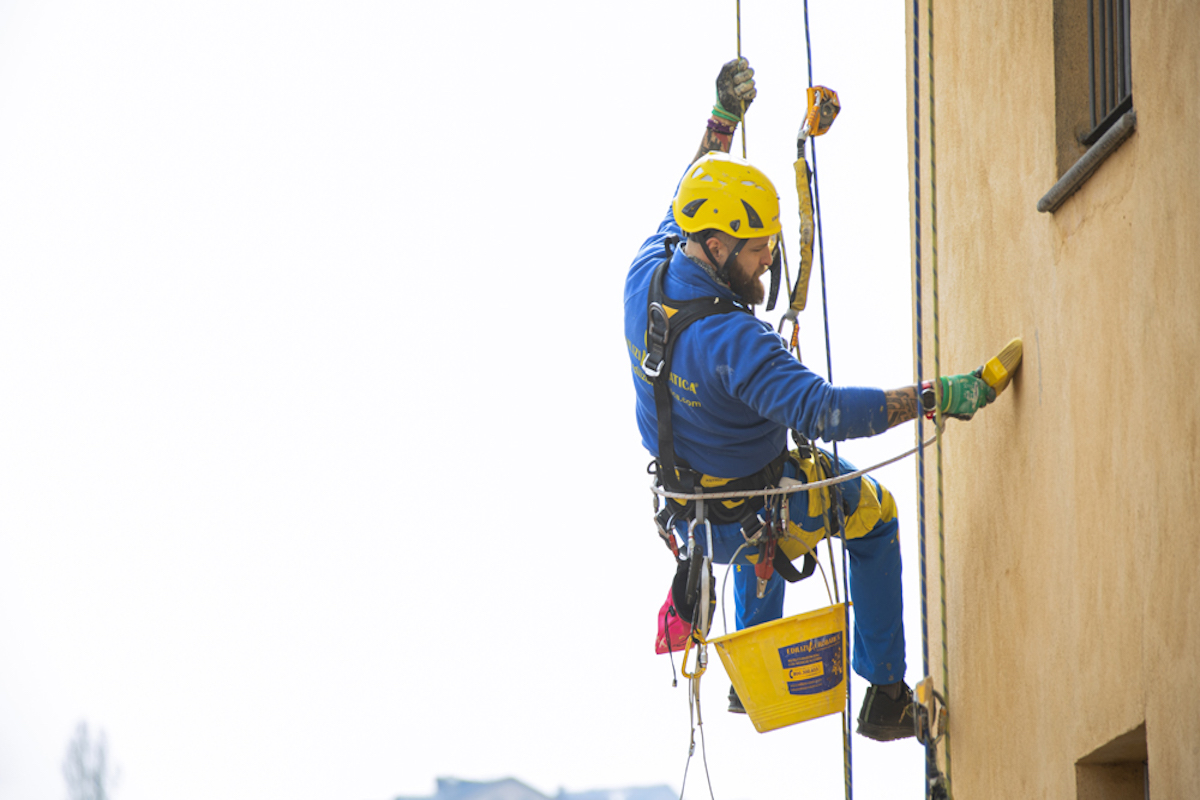 operaio Acrobatica durante tinteggiatura di una facciata