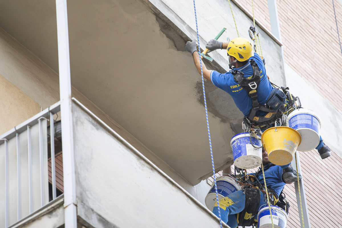 Operaio Acrobatica su fune durante il rifacimento di balconi in un condominio 