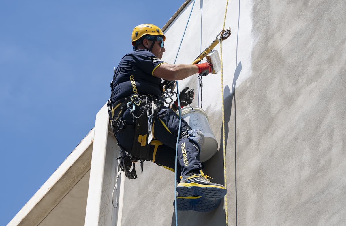 Operaio acrobatica su fune di profilo davanti a un condominio nell'intendo di rifacimento della sua facciata.